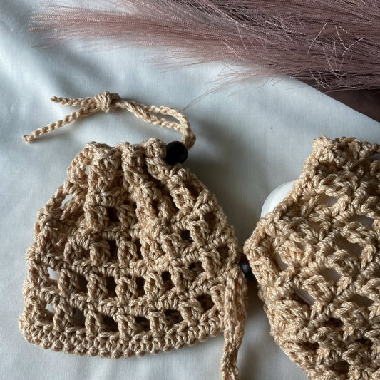 Two beige crochet items on a light surface with pink feathers in the background