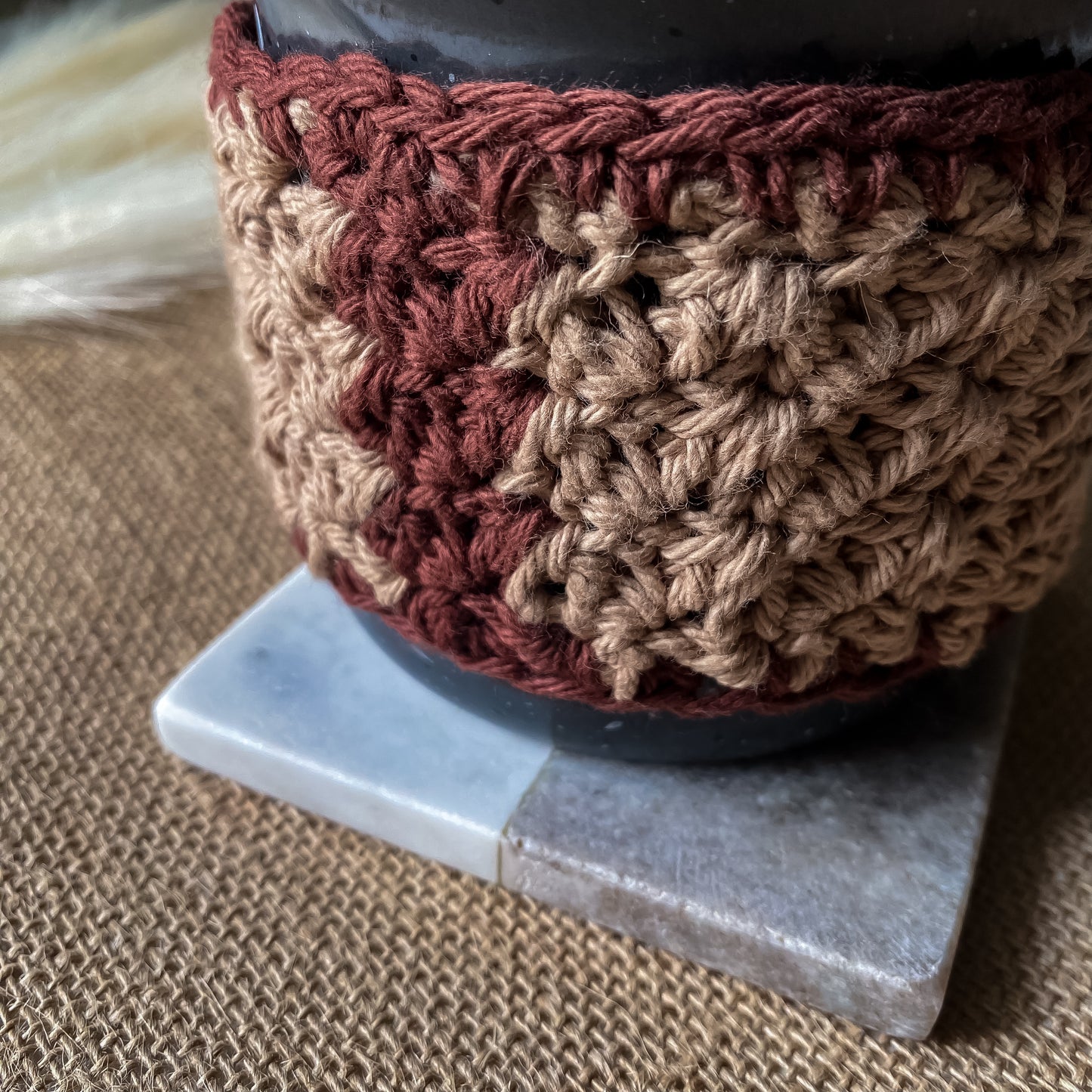 Close-up of a crocheted brown and red pot holder on a marble surface.