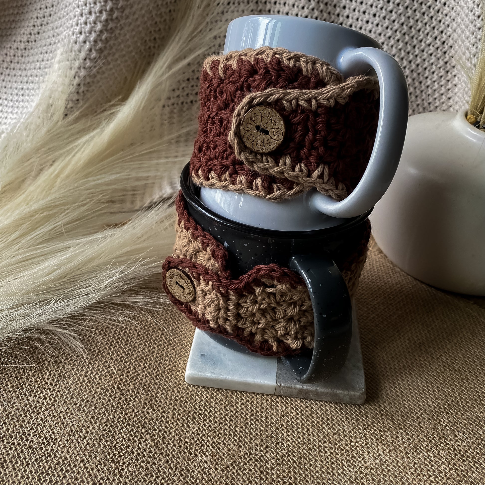 Two mugs with brown crochet cozies on a textured surface