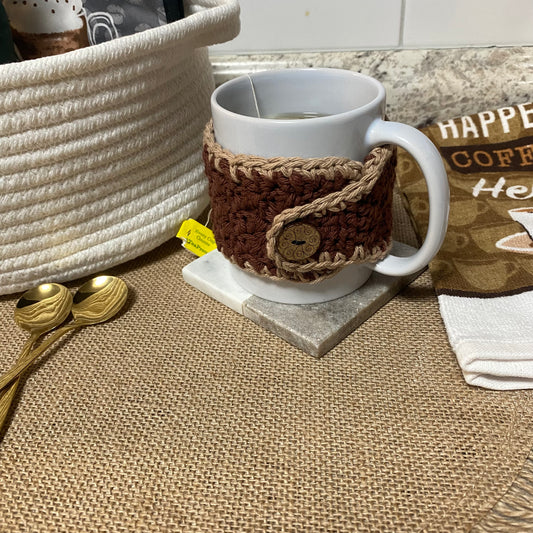 White mug with a brown textured cozy on a marble coaster, surrounded by kitchen items.