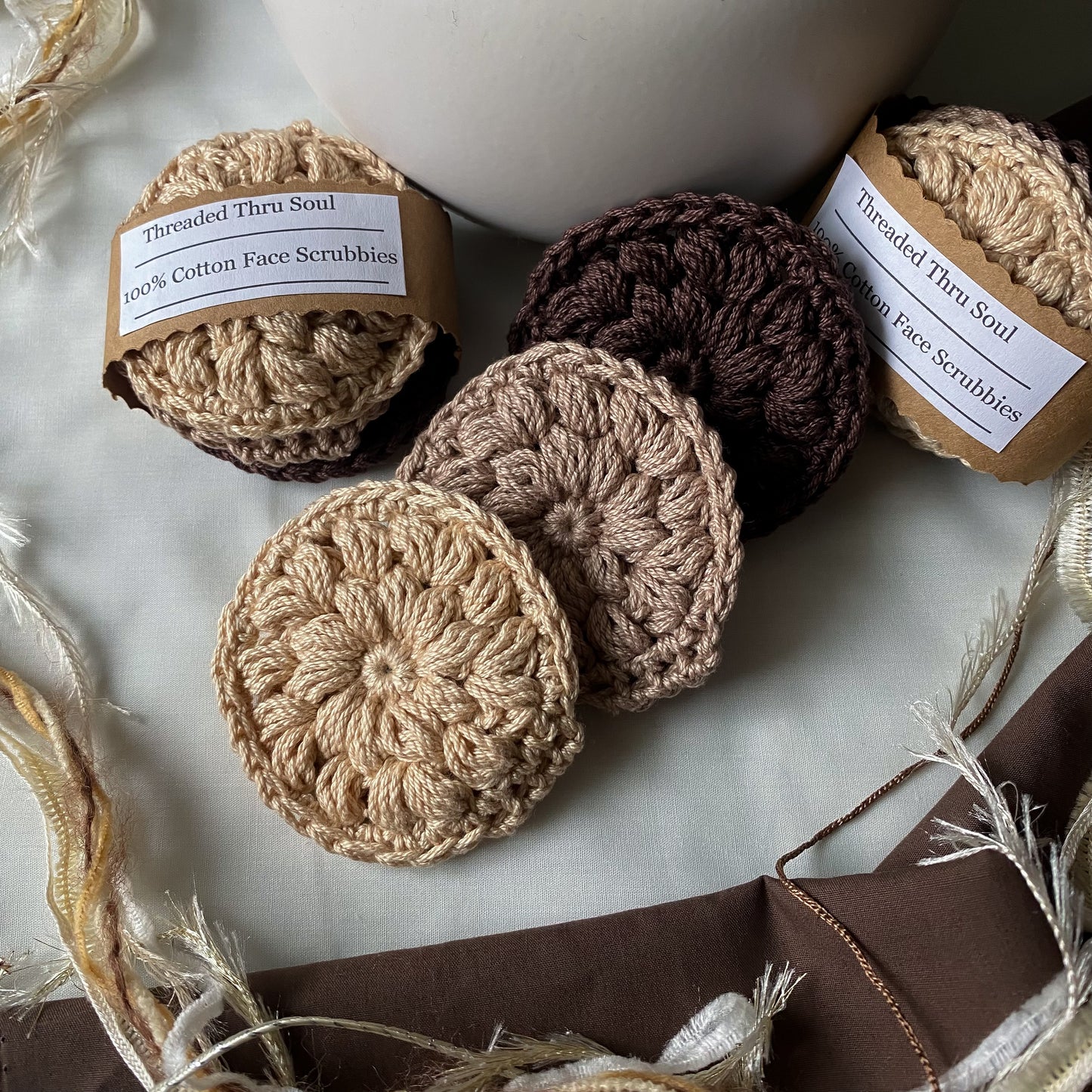Crocheted face scrubbies with 'Threaded Thru Soul' labels on a marble surface.